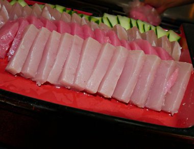 Kırmızı bir tabakta ton balığı sashimi dilimleri ve salatalık dilimleri