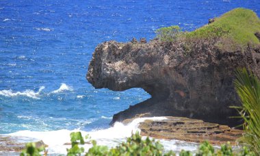 Tropik bir plajda bir köpeğin açık ağzını andıran büyük bir kayalık kayalık ile doğal kıyı görünümü, gökyüzü, 