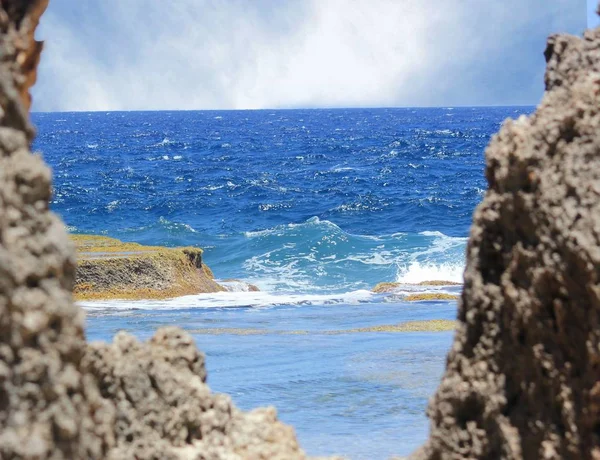 熱帯の島のぼやけた岩窓枠から見た海岸に転がる美しい青い海 — ストック写真