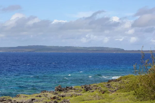Different hues of blue ocean seen from a rocky coral bank with green grass in a tropical island. Seen in