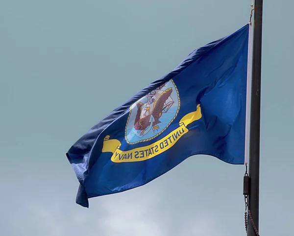 United States Navy flag waving in the wind from a pole, with light blue background