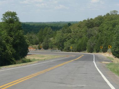 Arka planda yeşil ormanlar ve yeşillikile tehlike işaretleri ile Doğal kavisli yol