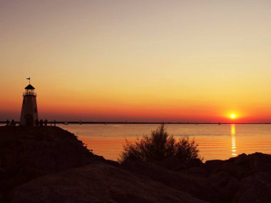 Bir deniz feneri siluetleri ile su üzerinde güzel gün batımı, insanlar ve tekneler yelken