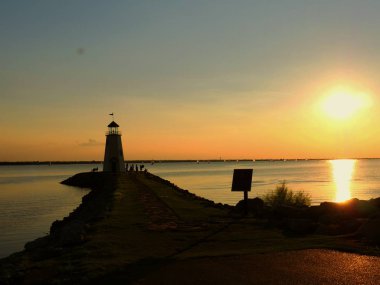 Güzel bir gün batımı ile siluetli bir deniz feneri, etrafında insanların siluetleri ile