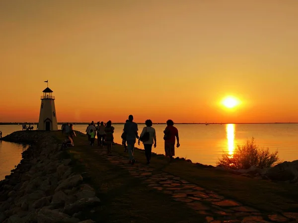 Tanınmayan insanların siluetleri gün batımında Oklahoma City'deki Hefner Gölü'ndeki deniz fenerine akın ediyor. 