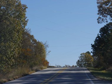 Yukarı doğru eğimli asfalt bir yol, ağaçların yapraklarının renkleri ile