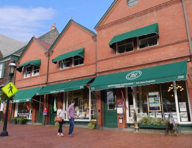 Newport, Rhode Island-September 2017: Attractive storefronts of establishments with a couple of tourists walking infront at Bellevue Avenue. clipart