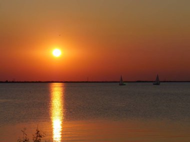 Gölde nefes kesici bir gün batımı. Suya yansıyan ışınlarla. Uzaktaki yelkenlilerle..