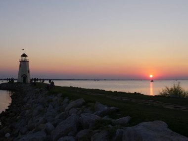 Uzaklarda güzel bir gün batımı olan deniz fenerinin silueti.