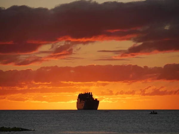 Medium wide shot of skies on fire at sunset, with the silhouettes of ships in the distance