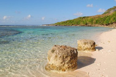 Kayalar, tropikal bir adada beyaz bir kumsalın güzelliğini artırır.