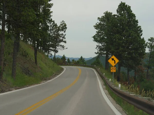 Roadside signs with speed direction along a sharp curve in the road at Custer State Park, South Dakota.