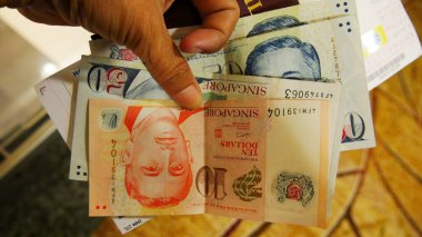 Singapore, Singapore-March 2016: Singapore dollar bills in varius amounts held by a hand, close up. clipart