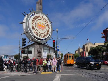 San Francisco, Kaliforniya-Temmuz 2018: İnsanlar, arka planda sarı bir tramvayla ünlü Balıkçı İskelesi tabelasının altında caddenin karşısına geçmek için kaldırımda bekliyorlar..