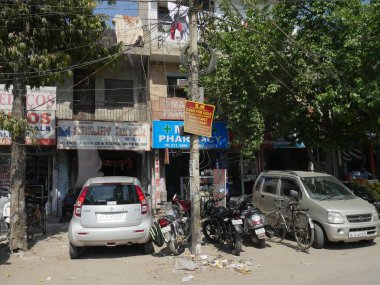 Yeni Delhi, Hindistan - Mart 2018: Arabalar ve motosikletler dükkanların önünde dar bir park alanı ve Yeni Delhi 'de bir eczane.
