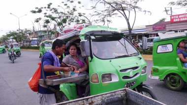 Tagum City, Filipinler- Mart 2016: Bir sigara satıcısı, Filipinler 'de popüler bir ulaşım biçimi olan motosikletli ve motosikletli yolculara satmaktadır.. 