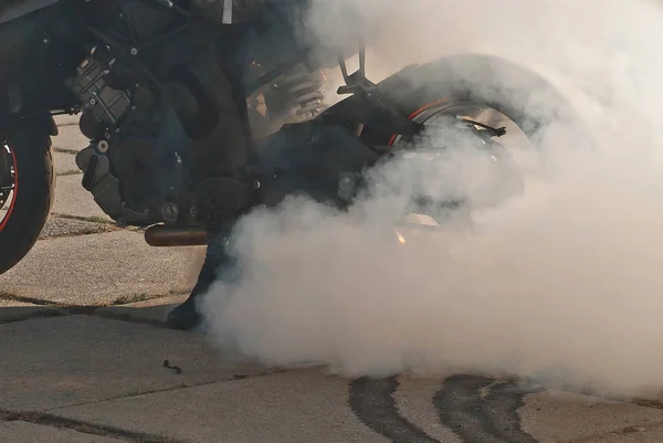 The smoke comes out from under the wheels. Motorcycle wheel closeup. Smoke due to tire rubbing against asphalt. The rider prepares to do the trick on the motorcycle. Burned rubber on the road.