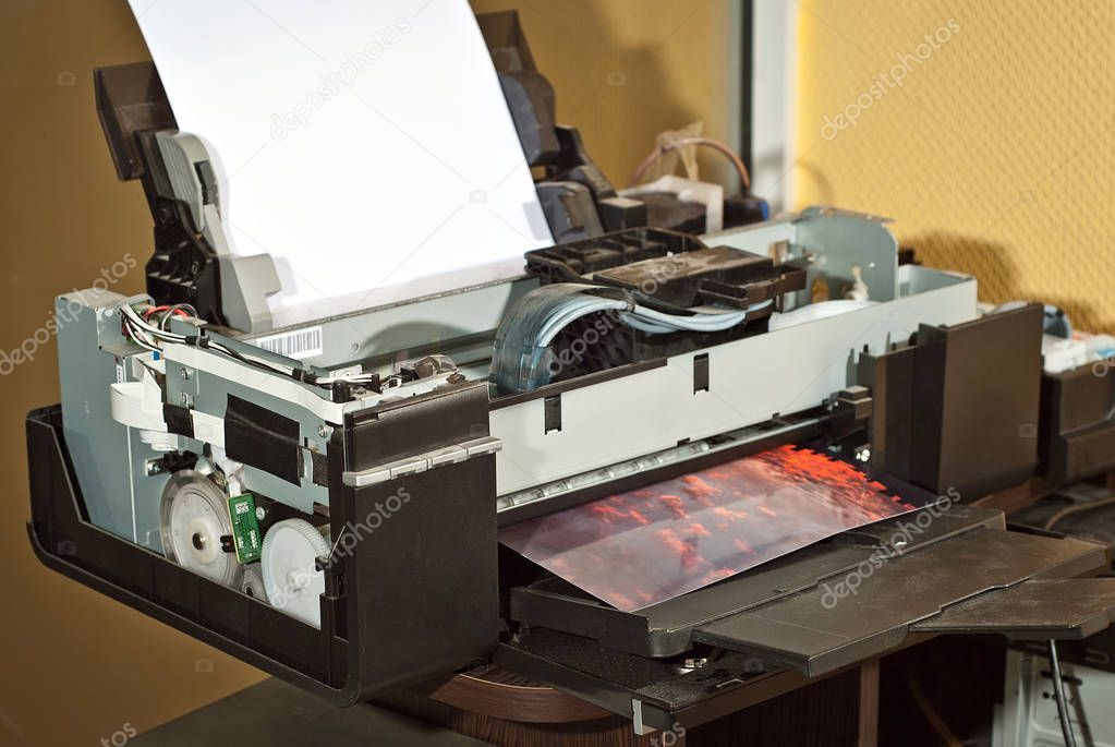 Old broken printer in workshop. The concept of cleaning and calibrating printers. Sunset and red sky with clouds in the photo. Picturesque nature photo printed on printing equipment.