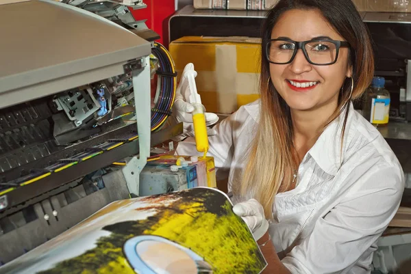 Girl in gloves fills the cartridge with paint. Woman repairing and servicing the printer. Yellow paint in syringe and hands close up. Assistant in white shirt and glasses.