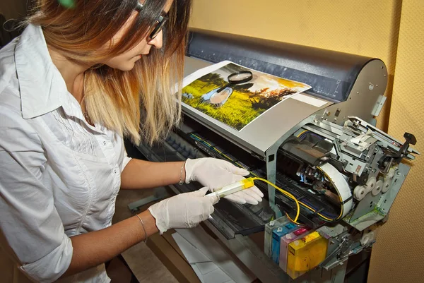 Girl in gloves fills the cartridge with paint. Woman repairing and servicing the printer. Yellow paint in syringe and hands close up. Assistant in white shirt and glasses.