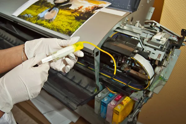 Girl in gloves fills the cartridge with paint. Woman repairing and servicing the printer. Yellow paint in syringe and hands close up.