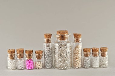 Beyaz, bej ve sarı boncuklar gri arka planda cam kavanozlarda. Tahta mantarlı şeffaf bir kabın içinde boncuklar..