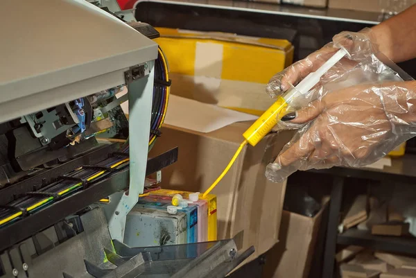 Girl in gloves fills the cartridge with paint. Woman repairing and servicing the printer. Yellow paint in syringe and hands close up.