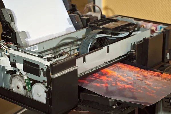 Old broken printer in workshop. The concept of cleaning and calibrating printers. Sunset and red sky with clouds in the photo. Picturesque nature photo printed on printing equipment.