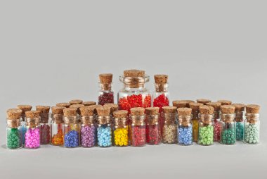 Kırmızı, sarı, mavi, yeşil, mor, pembe ve turuncu boncuklar gri arka planda cam kavanozlarda. Tahta mantarlı şeffaf bir kabın içinde boncuklar. Düzen, denge ve kaos kavramı..