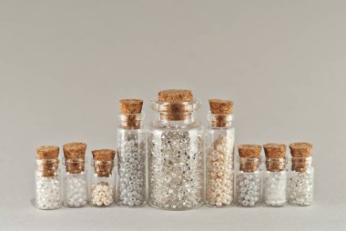 Beyaz, bej ve sarı boncuklar gri arka planda cam kavanozlarda. Tahta mantarlı şeffaf bir kabın içinde boncuklar..