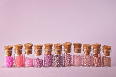 Parlak mor arka planda cam kavanozlarda bej, pembe ve sarı boncuklar. Tahta mantarlı şeffaf bir kabın içinde boncuklar. Düzen, denge ve kaos kavramı..