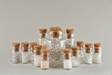 Beyaz, bej ve sarı boncuklar gri arka planda cam kavanozlarda. Tahta mantarlı şeffaf bir kabın içinde boncuklar..