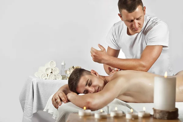 白いTシャツのマッサージセラピストが背中のマッサージをしています その男は白い背景のテーブルの上に横たわっている 手動療法 — ストック写真