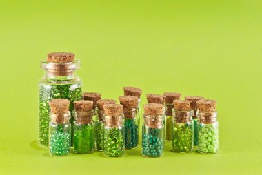 Yeşil ve sarı boncuklar parlak yeşil arka planda cam kavanozlarda. Tahta mantarlı şeffaf bir kabın içinde boncuklar..