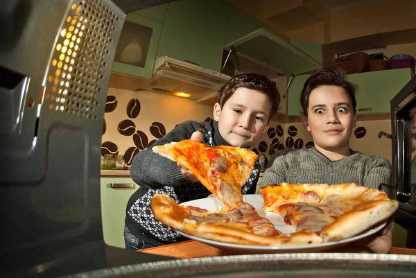 The guys get pizza from the microwave. Food heating in the home kitchen. Fast food. Mid-view view of microwave. Cooking at home. Pizza and burgers are removed from the oven. Kids eating pizza.