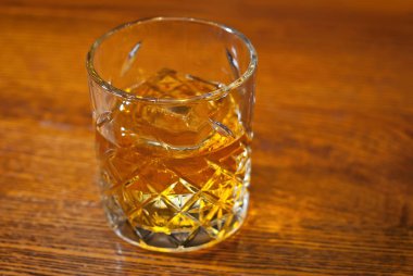 Bar tezgahında sarı kokteyl. Barın arka planında viski, rom ya da brendi. Ahşap bir tahtanın üzerinde içki bardağı.