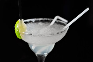 Bar tezgahında beyaz kokteyl. Martini, cin, tekila ve limonla birlikte iç. Siyah arka planda içki bardağı. Buzlu kokteyl yakın plan..