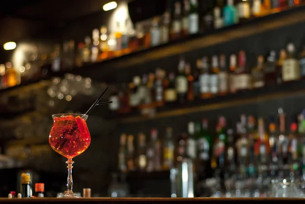 バーカウンターで赤いカクテル アルコールとボトルの背景にマティーニ ラム酒 テキーラとフルーツを飲みます 板に酒を盛ったガラス — ストック写真