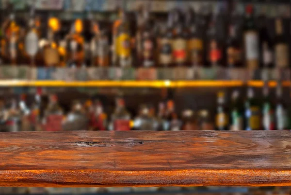 Wooden board on a background of bottles with alcohol. Old bar counter as layout for design. Workpiece for design. Empty place to advertise products. Blurred interior of the bar in the background.