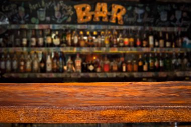 Wooden board on a background of bottles with alcohol. Old bar counter as layout for design. Workpiece for design. Empty place to advertise products. Blurred interior of the bar in the background. clipart