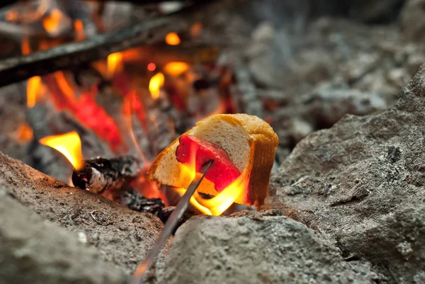 A piece of meat and bread is fried on fire. Bread on skewers near bonfire. Cooking on a hike.