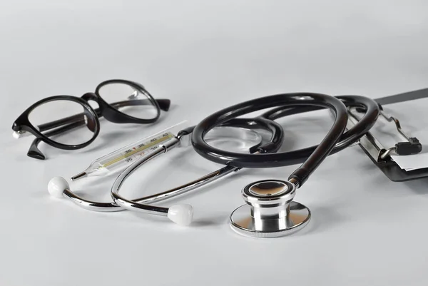 Medical equipment on a white background. Stethoscope, glasses, thermometer near black folder.