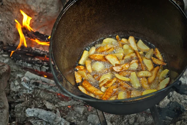 Potatoes are cooked in a large pot on fire. Food is cooked on a campfire in marching conditions.