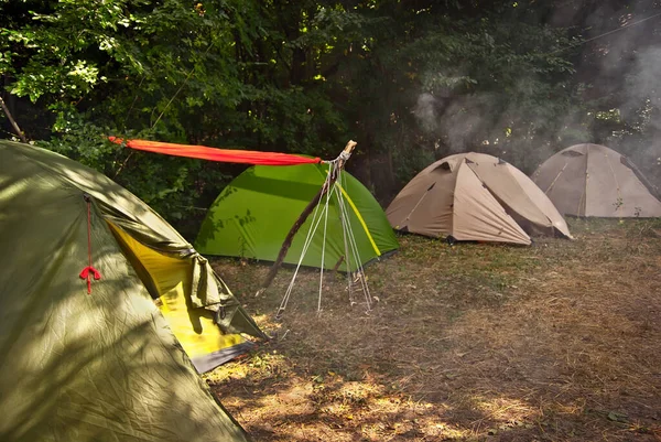 テントを張れテントの間にオレンジハンモックが伸びています テントの上の煙のキャンプファイヤー — ストック写真