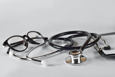 Beyaz arka planda gözlüklü ve klasörlü steteskop. Tıbbi malzemeler masada..