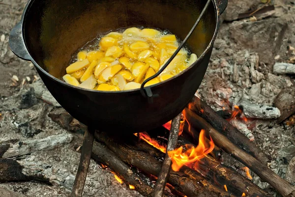 Potatoes are cooked in a large pot on fire. Food is cooked on a campfire in marching conditions.