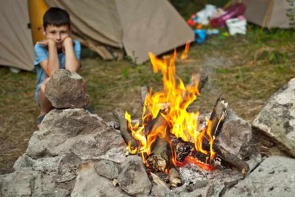 少年は火のそばに座っている 高温でシャープです テントの上で赤ちゃん — ストック写真