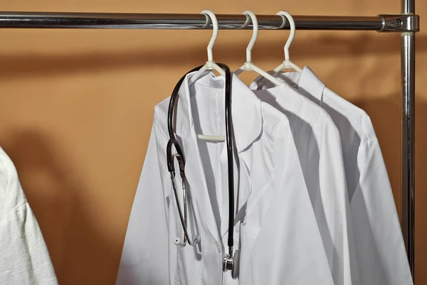 Askıda Beyaz Tıbbi Elbiseler Asılı Turuncu Arka Planda Steteskoplu Kıyafetler — Stok fotoğraf