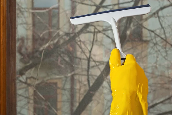黄色のゴム手袋で手を閉じます 掃除機が窓を洗う シャープに汚れたほこりっぽいガラス 窓の外の街の通りや建物 建築物は背景がぼやけている — ストック写真
