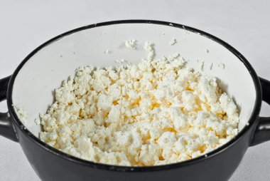 Siyah kasede beyaz süzme peynir. Beyaz arka planda bir sürü peynir.